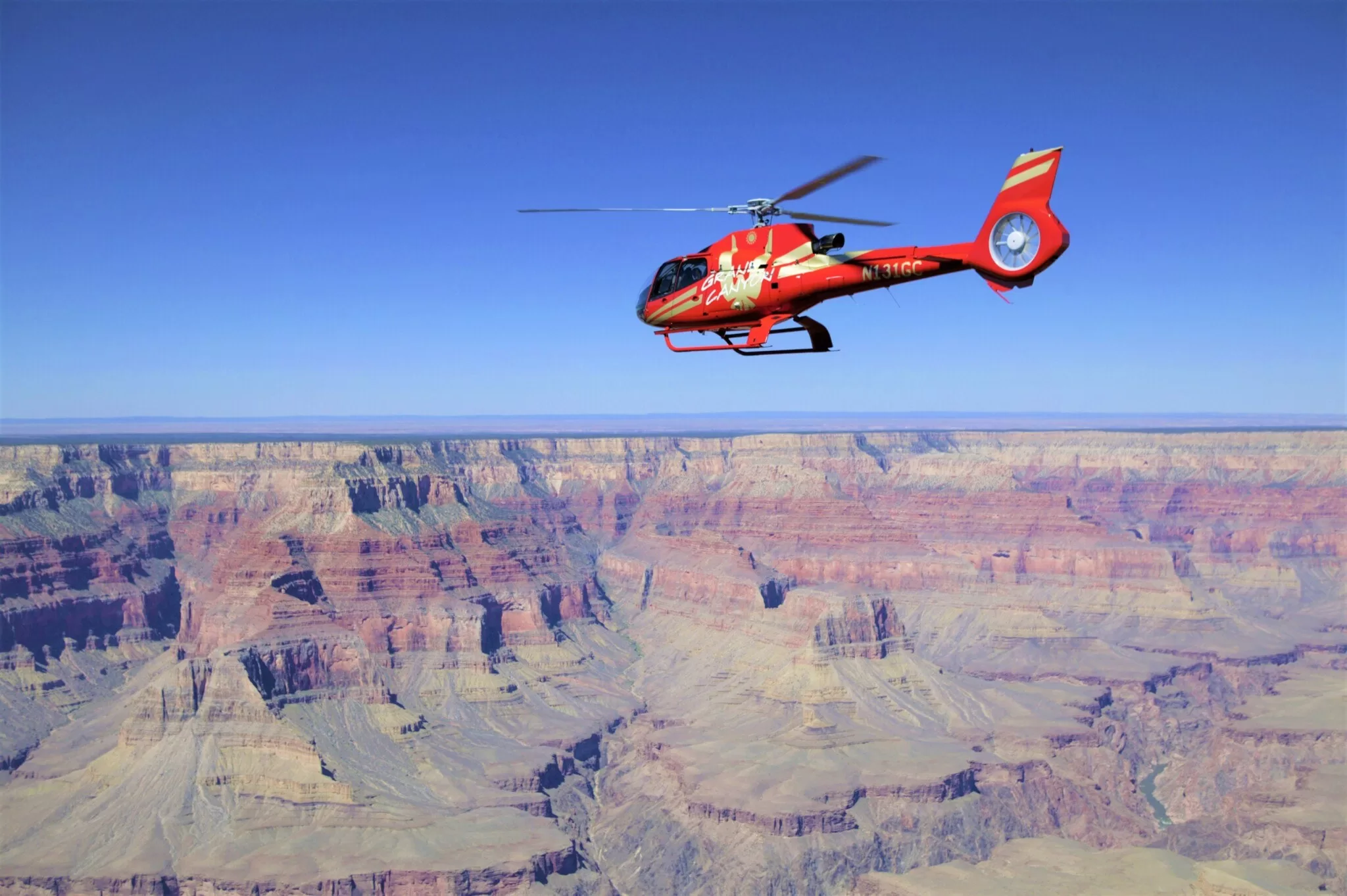 Roter Hubschrauber fliegt über den Grand Canyon National Park und überblickt Felsformationen und Schluchten