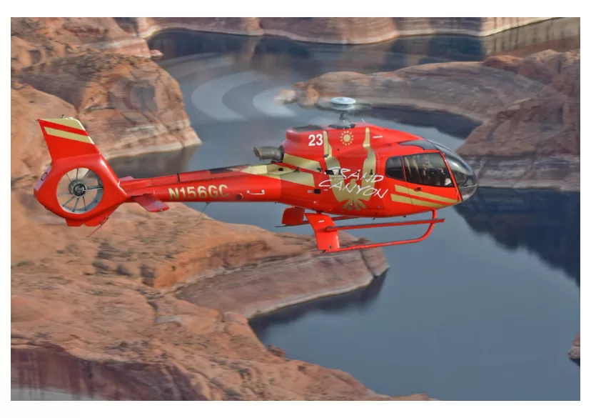 Rot-goldener Hubschrauber fliegt über Steinadler und runde orangefarbene Felsformationen in der Wüstenlandschaft.