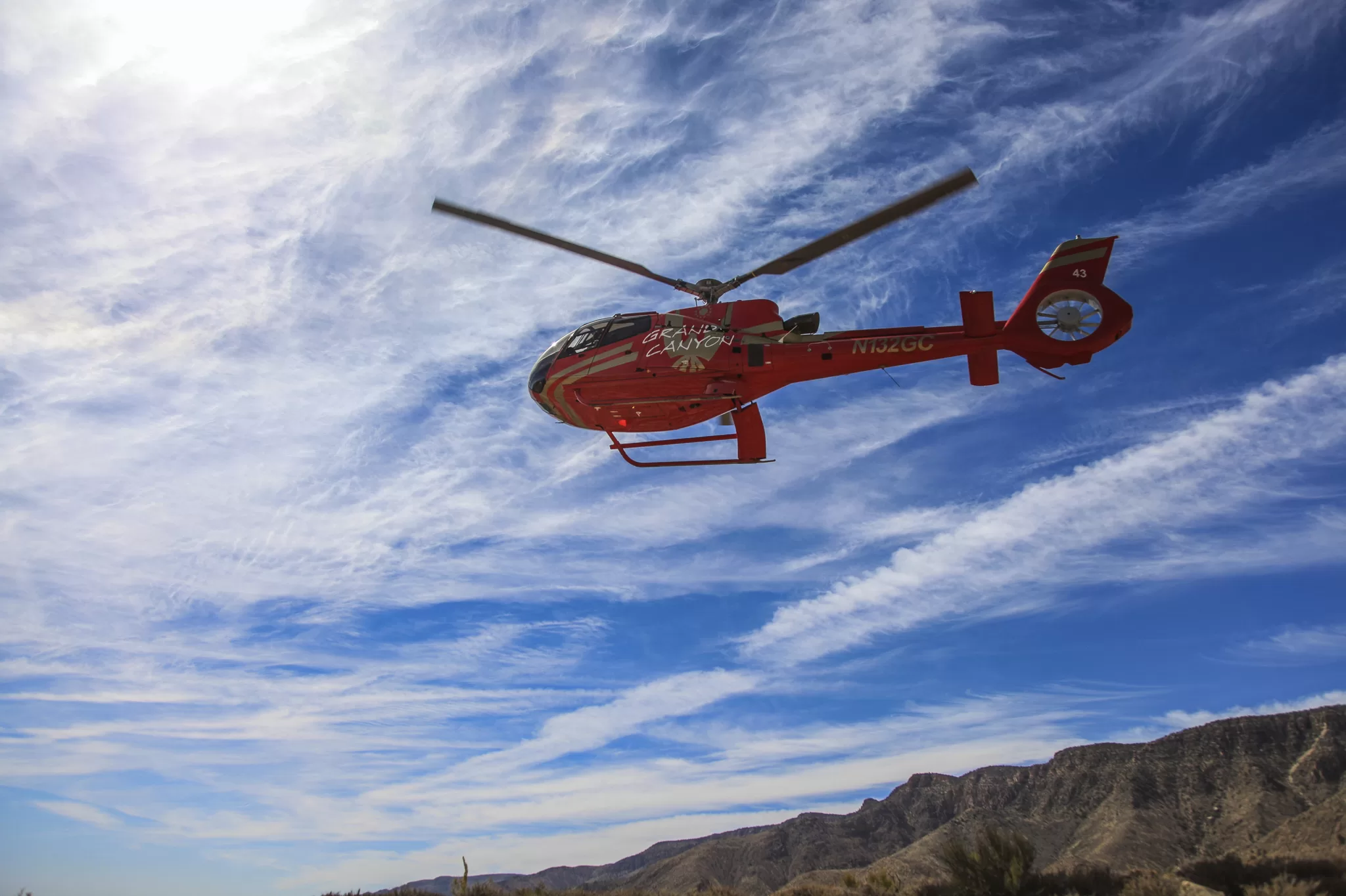Rot-goldener Hubschrauber, fotografiert vom Boden aus vor einem blauen, teilweise bewölkten Himmel