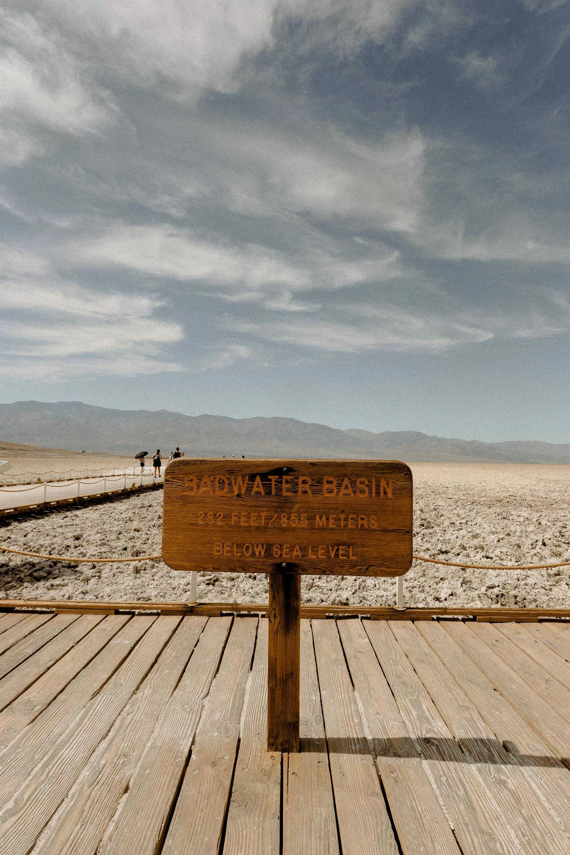 Hölzernes Schild am Badwater Basin im Death Valley, 282 Fuß unter dem Meeresspiegel, trockene Salzlandschaft und Wanderweg sichtbar