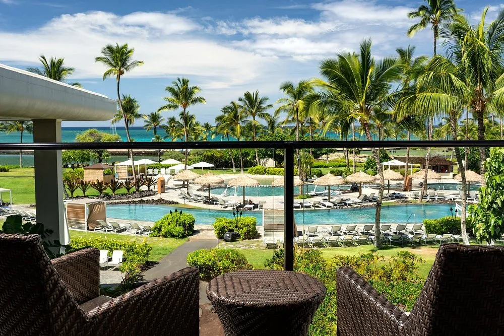 Uitzicht vanaf een balkon over een buitenzwembad met de zee op de achtergrond bij het Hotel Waikoloa Beach Marriott Resort Spa Waikoloa