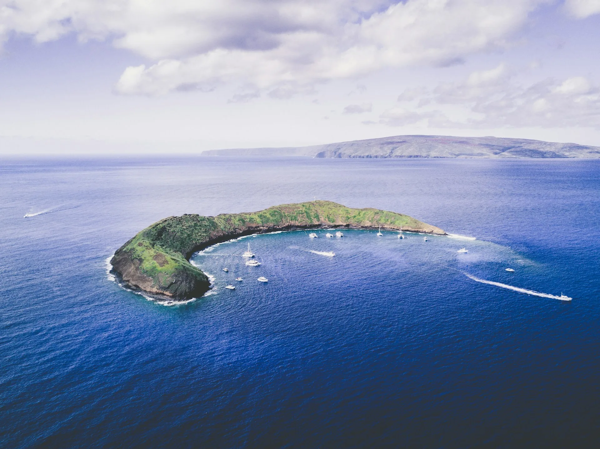 Het kleine, cikkelvormige eiland Molokini met boten in het water
