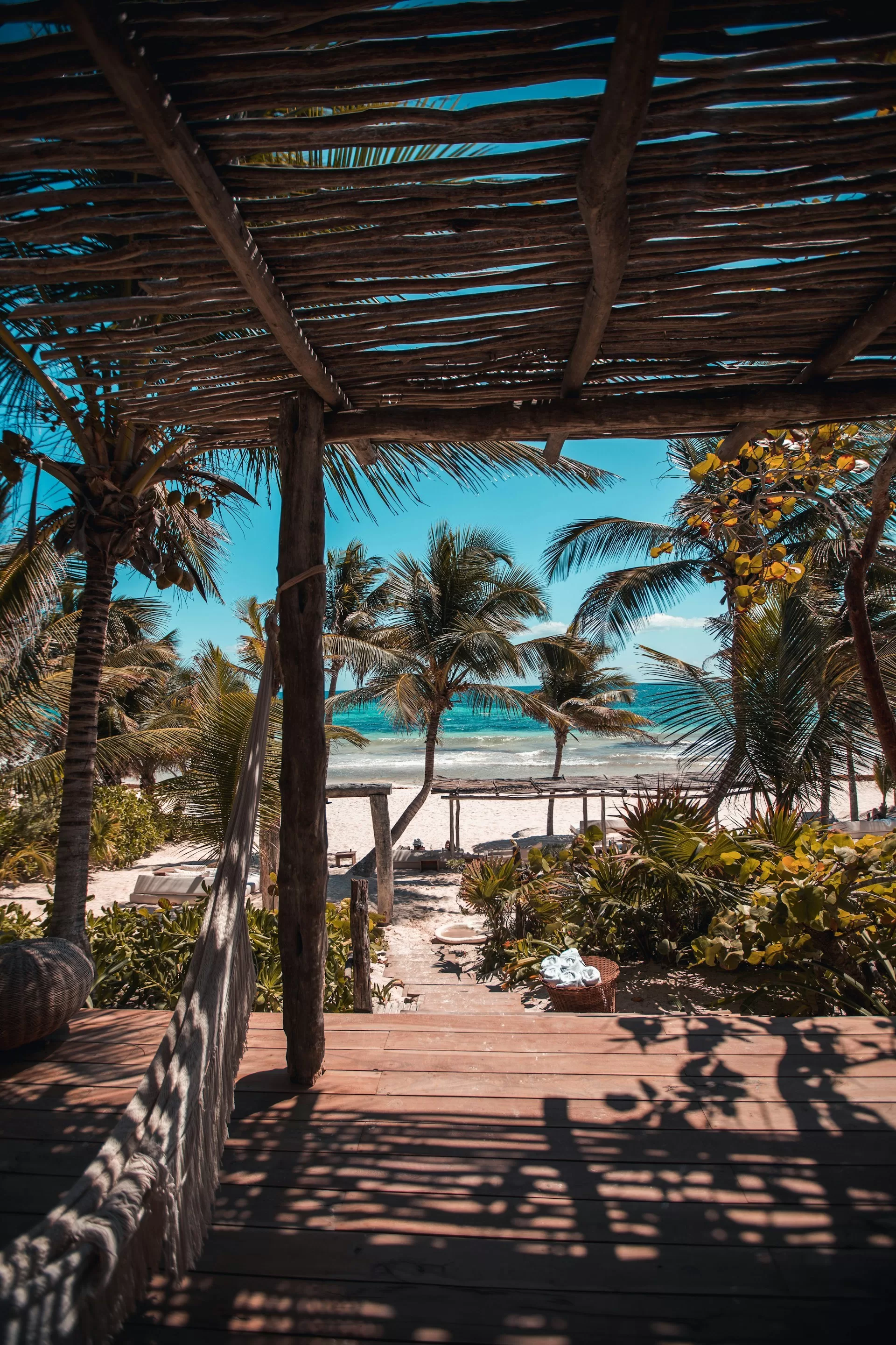 Uitzicht vanonder een houten cabana met hangmat op het witte strand van Tulum, Mexico