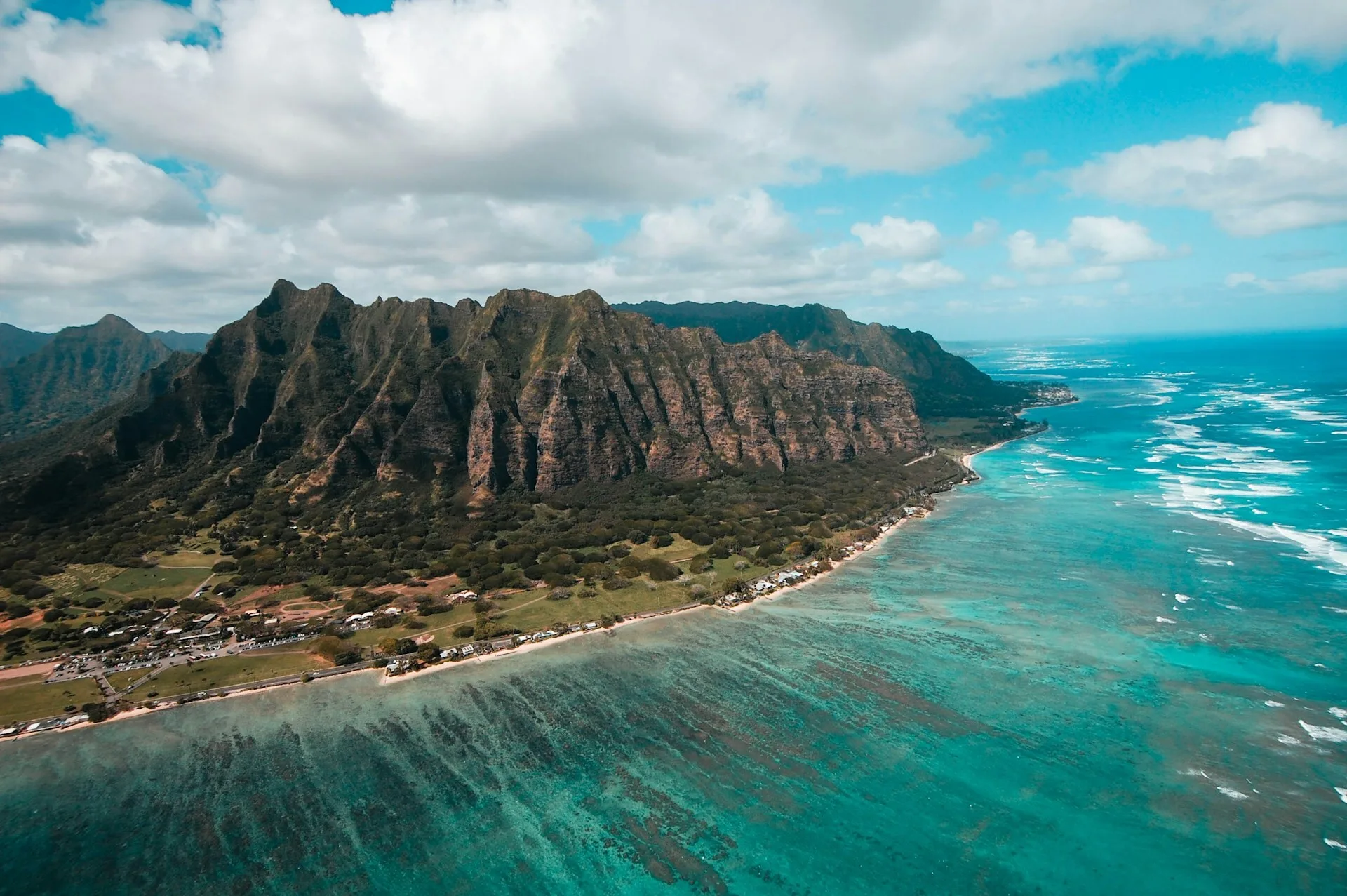 Luftaufnahme von Oahu, Hawaii, mit grün bewachsenen Felsen, dem Meer im Vordergrund und einem Dorf in der Ferne