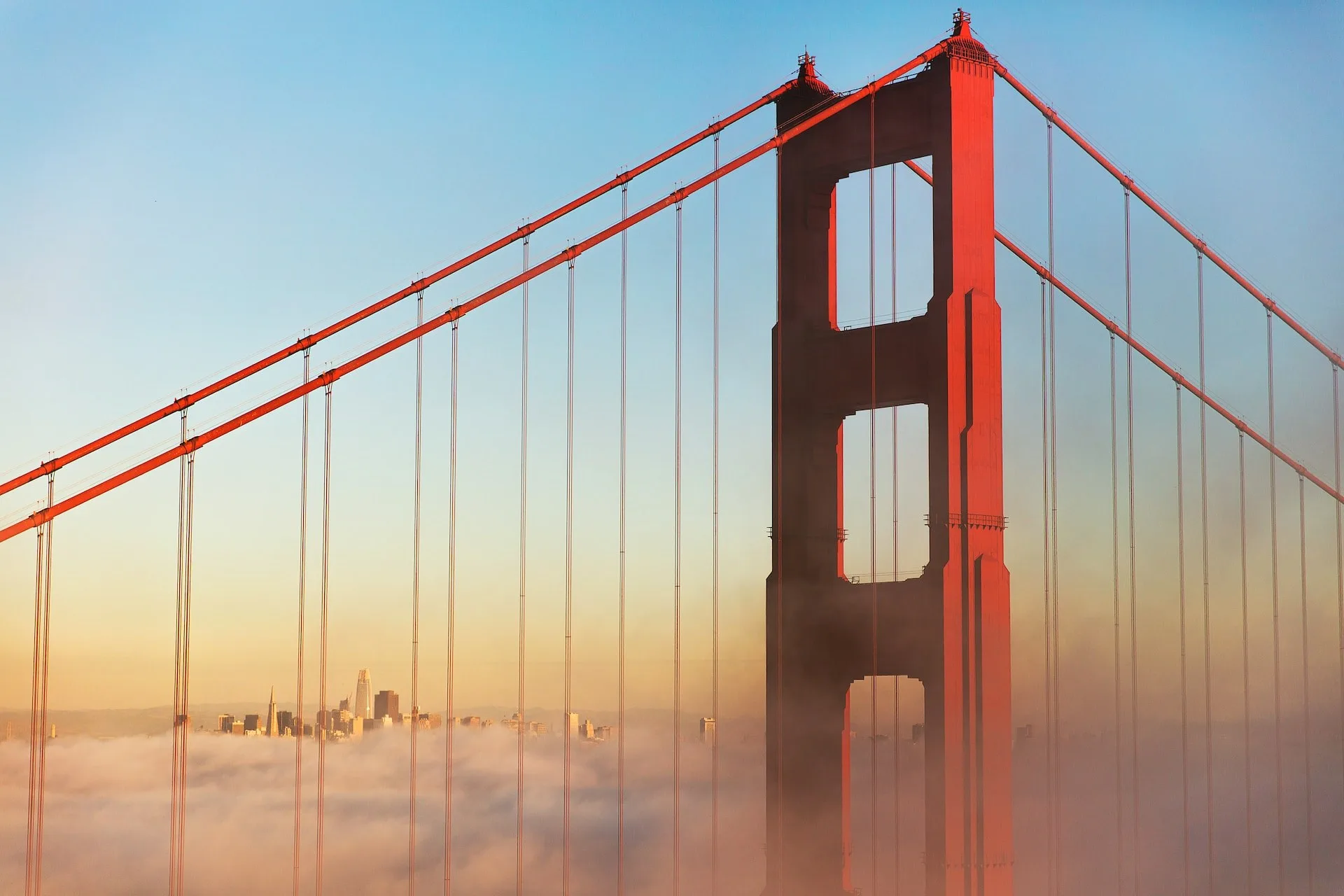 De top van de Golden Gate Bridge in mist gehuld met de skyline van San Francisco op de achtergrond
