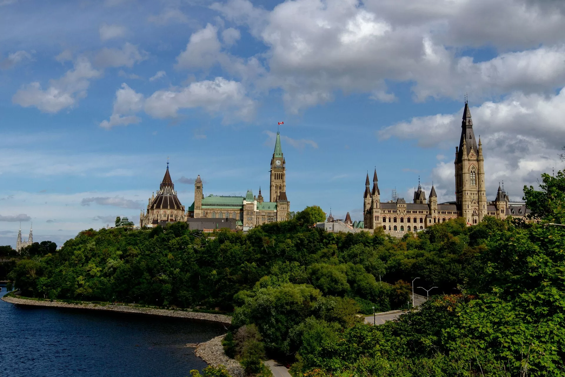 Parliament Hill mit Wald und Wasser im Vordergrund, rechts ist eine Kirche deutlich in der Landschaft zu erkennen