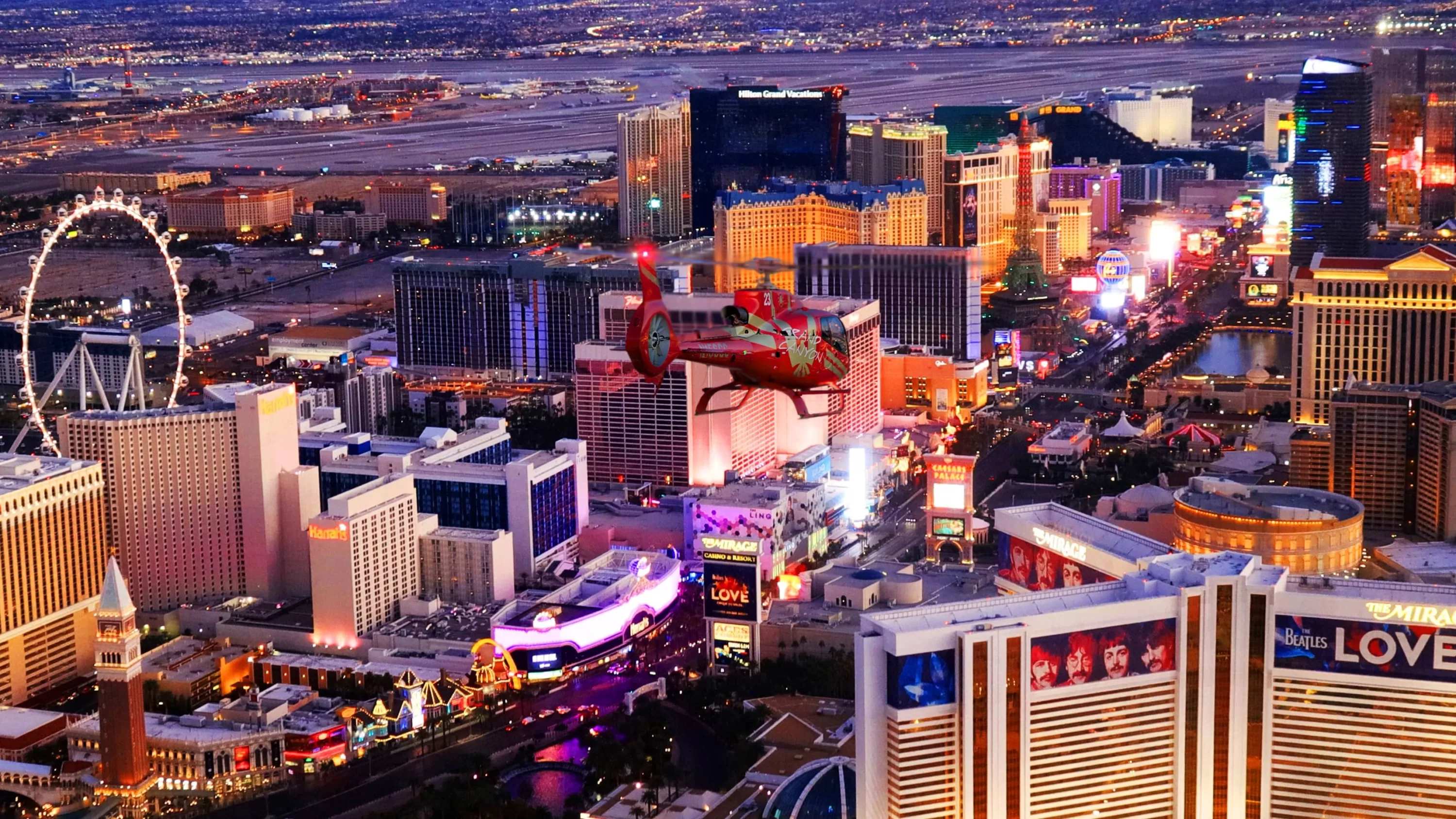 Rot-goldener Hubschrauber fliegt bei Sonnenuntergang über den Strip in Las Vegas mit Mini-Eiffelturm und London Eye im Blick