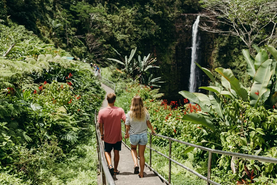 Een stelletje loopt op een wandelpad naast een waterval in Akaka Falls State Park op Big Island
