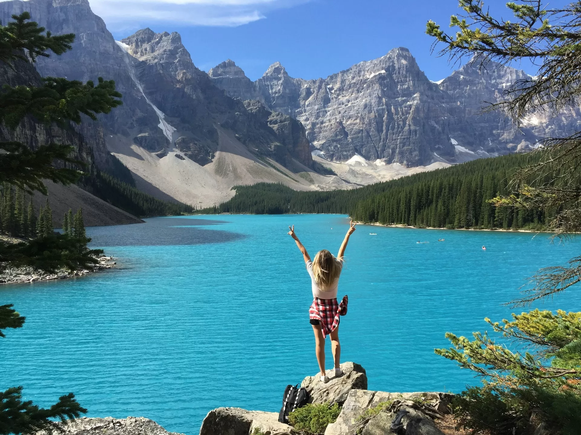Vrouw met uitgestrekte armen voor een turquoise meer in West Canada