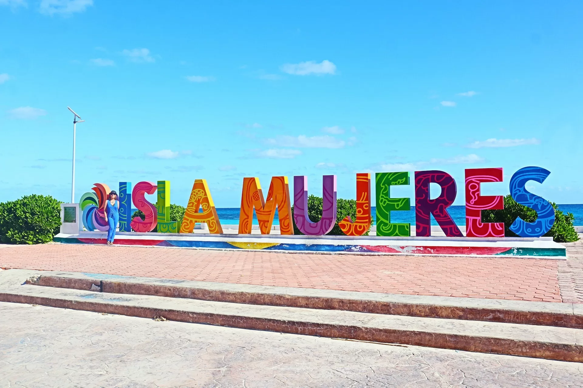 Het sign Isla Mujeres in gekleurde letters met poserende vrouw en de zee op de achtergrond.